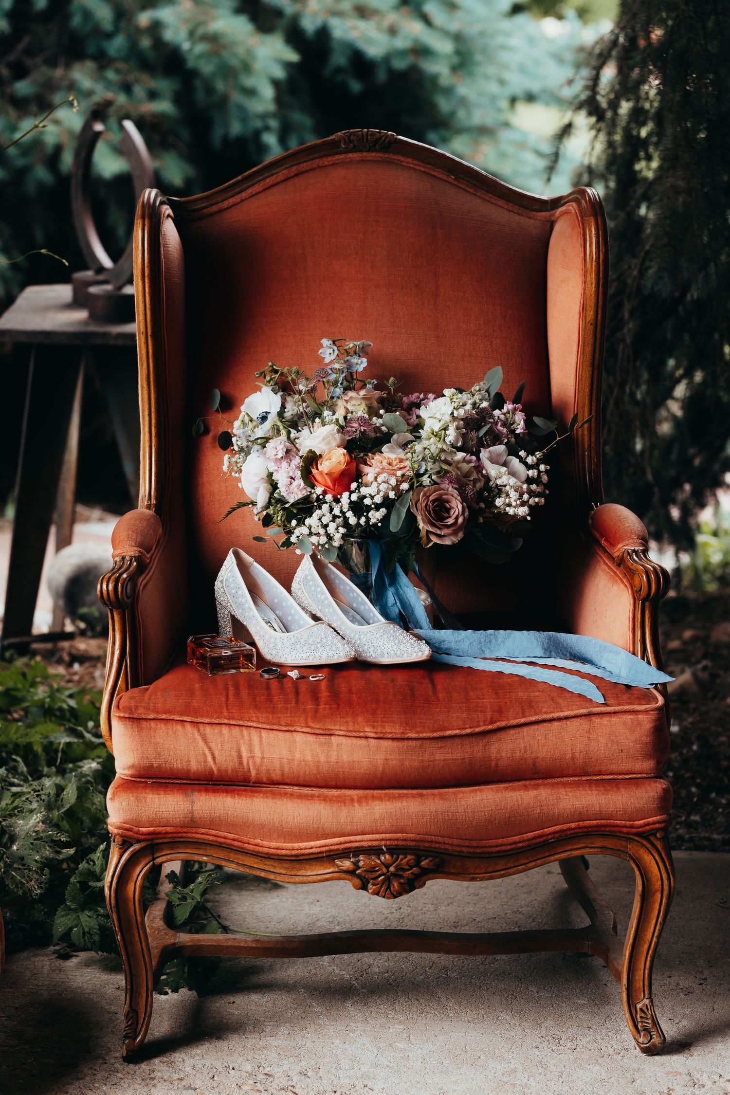 Vintage orange armchair with bridal bouquet and white heels arranged for wedding photography.