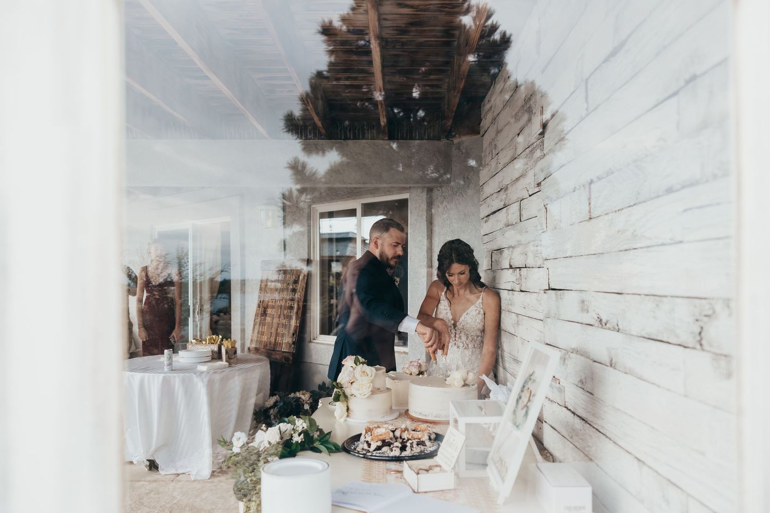 A rustic white wood paneled room decorated for a wedding reception with dessert table.