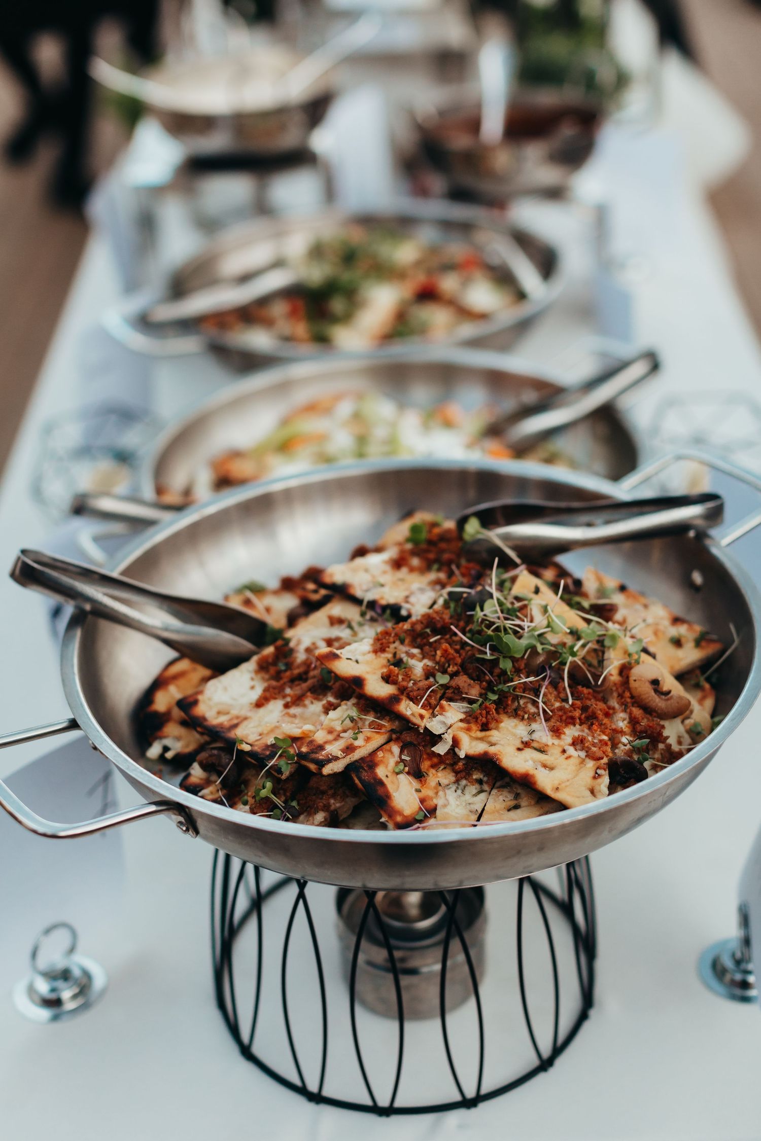 Elegant wedding buffet display featuring hot dishes in silver chafing dishes on decorative stands.