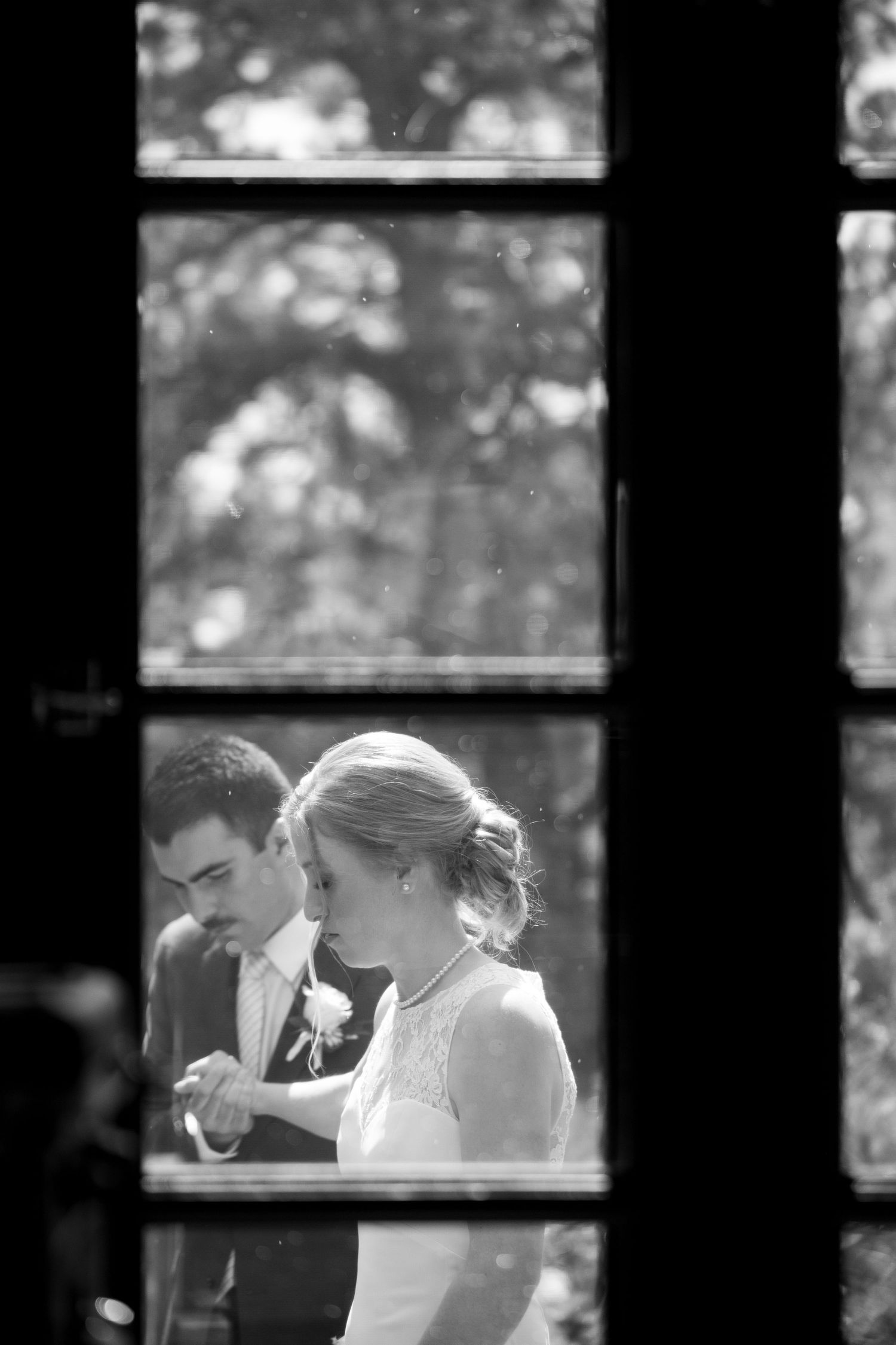 A romantic black and white wedding moment viewed through a window frame.