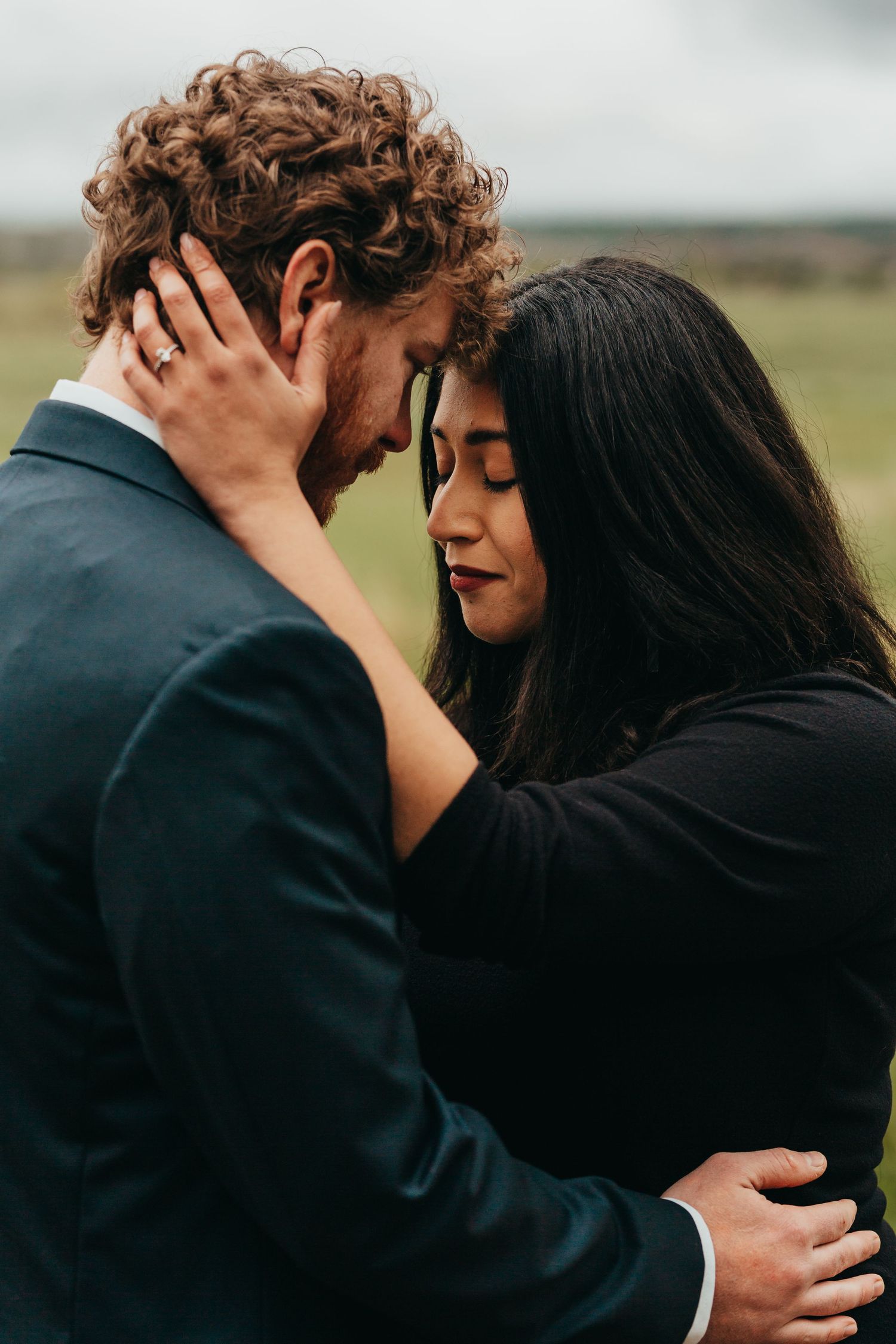 Intimate portrait of a couple sharing a tender moment against a moody outdoor backdrop.