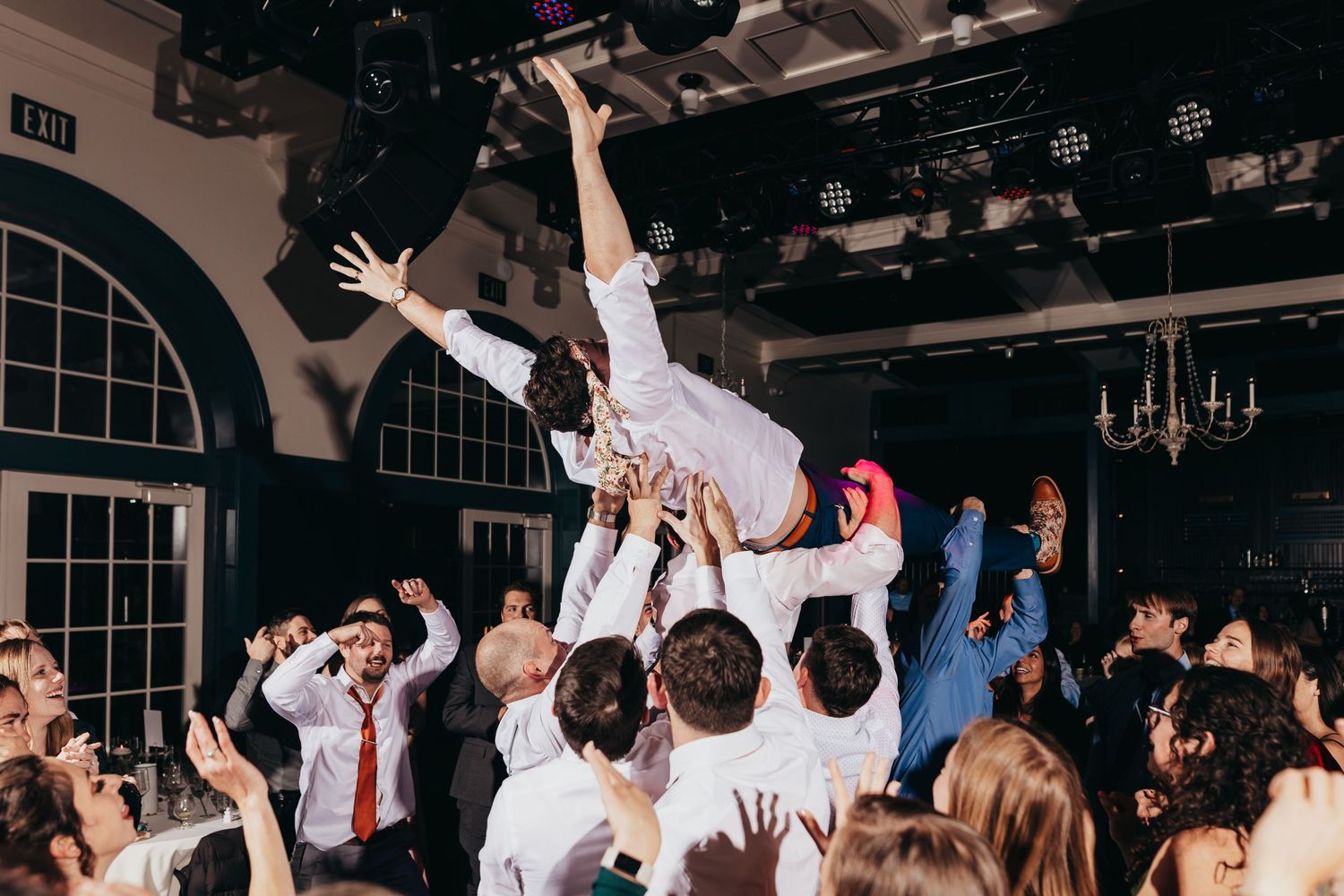 Wedding crowd lifting person horizontally during lively dance celebration.