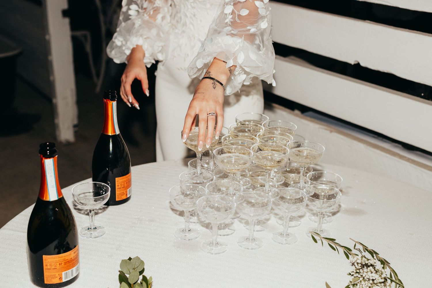 Champagne bottles and crystal glasses being arranged on white table at wedding reception.
