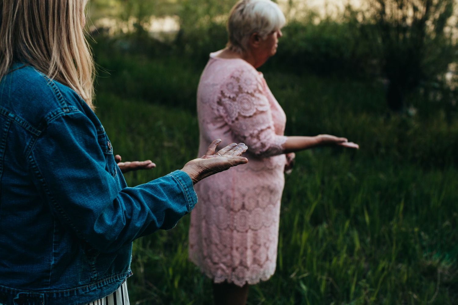 Two people standing in green field wearing pink and denim clothing.