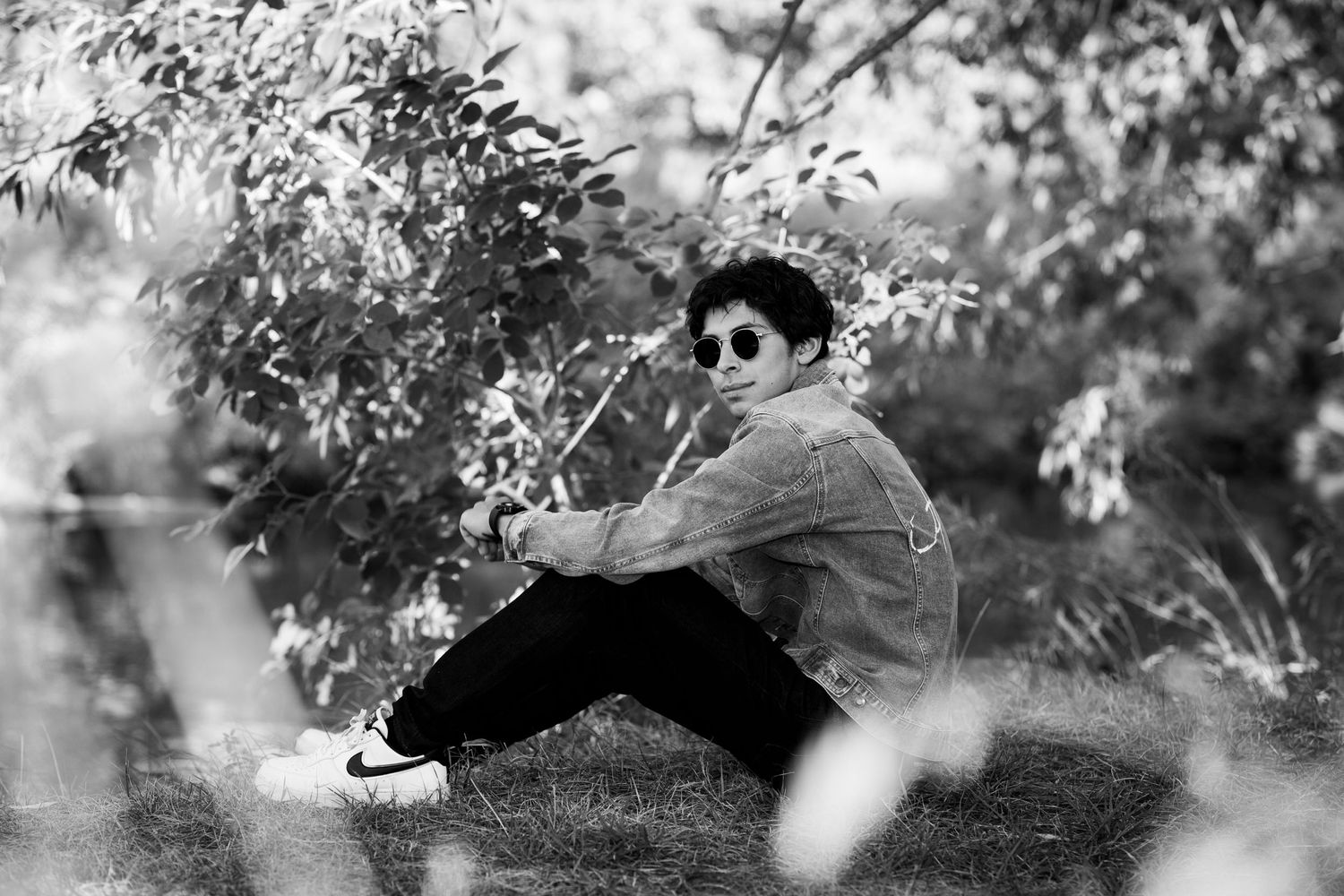 Artistic black and white portrait of person sitting under blooming tree branches.