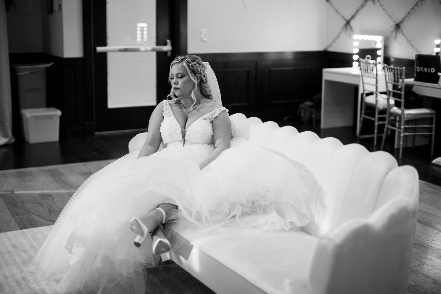 Black and white photo of a bride in a flowing white dress sitting on a bench.