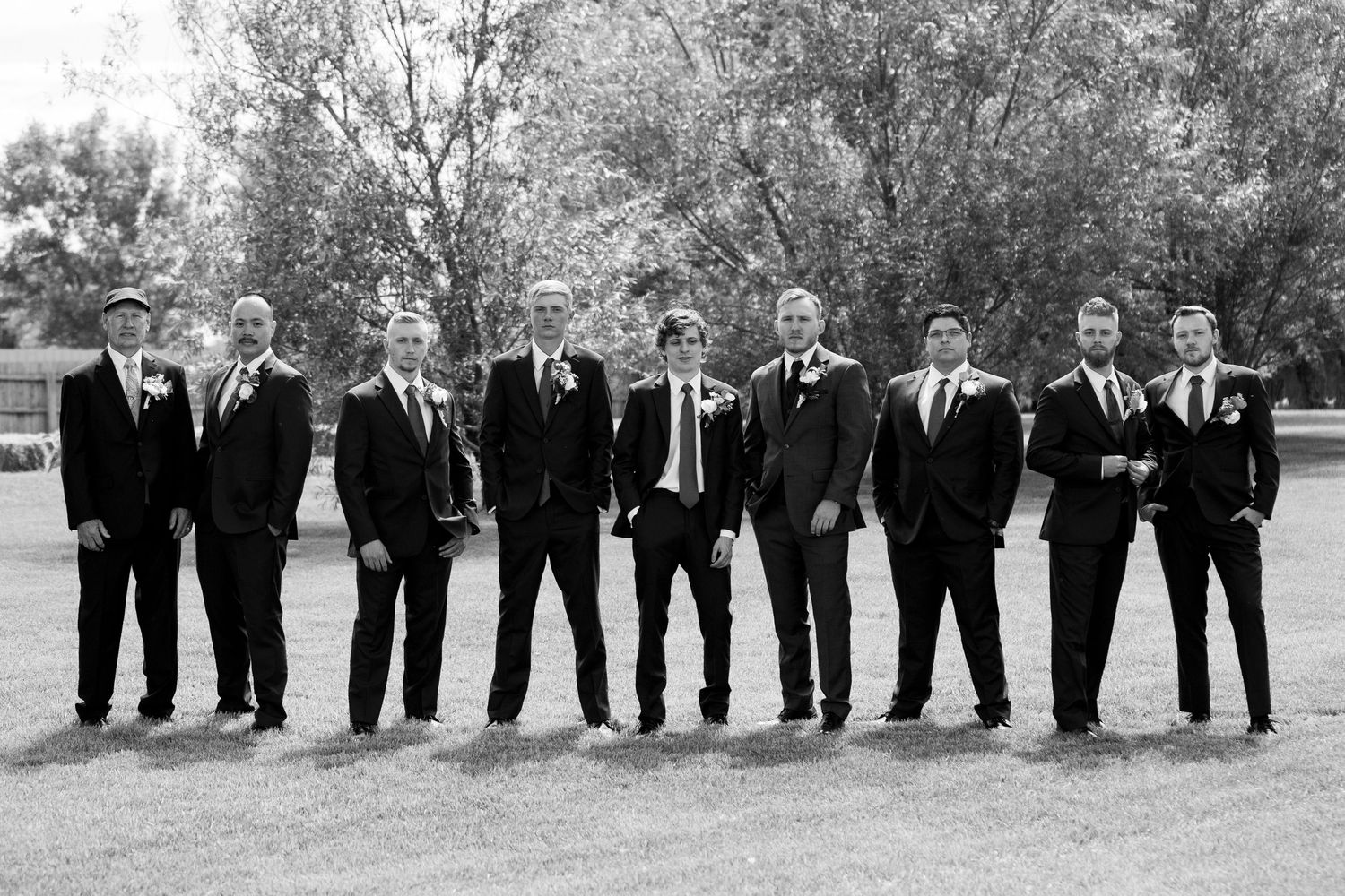 Wedding party groomsmen in black suits pose outdoors in classic black and white photo.