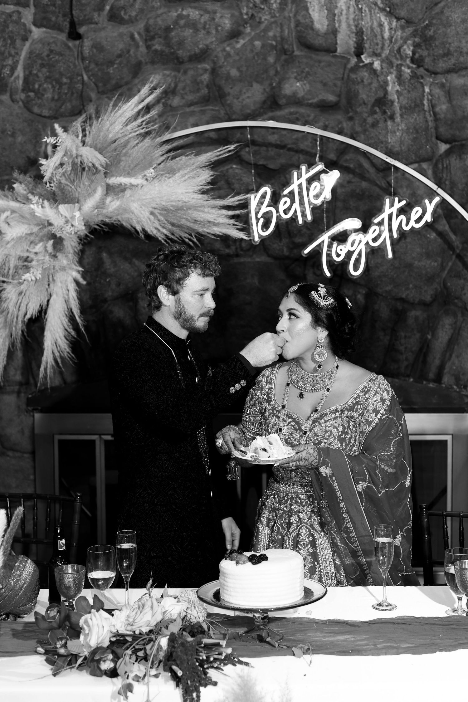 A vintage black and white wedding cake cutting moment under a 'Better Together' sign.