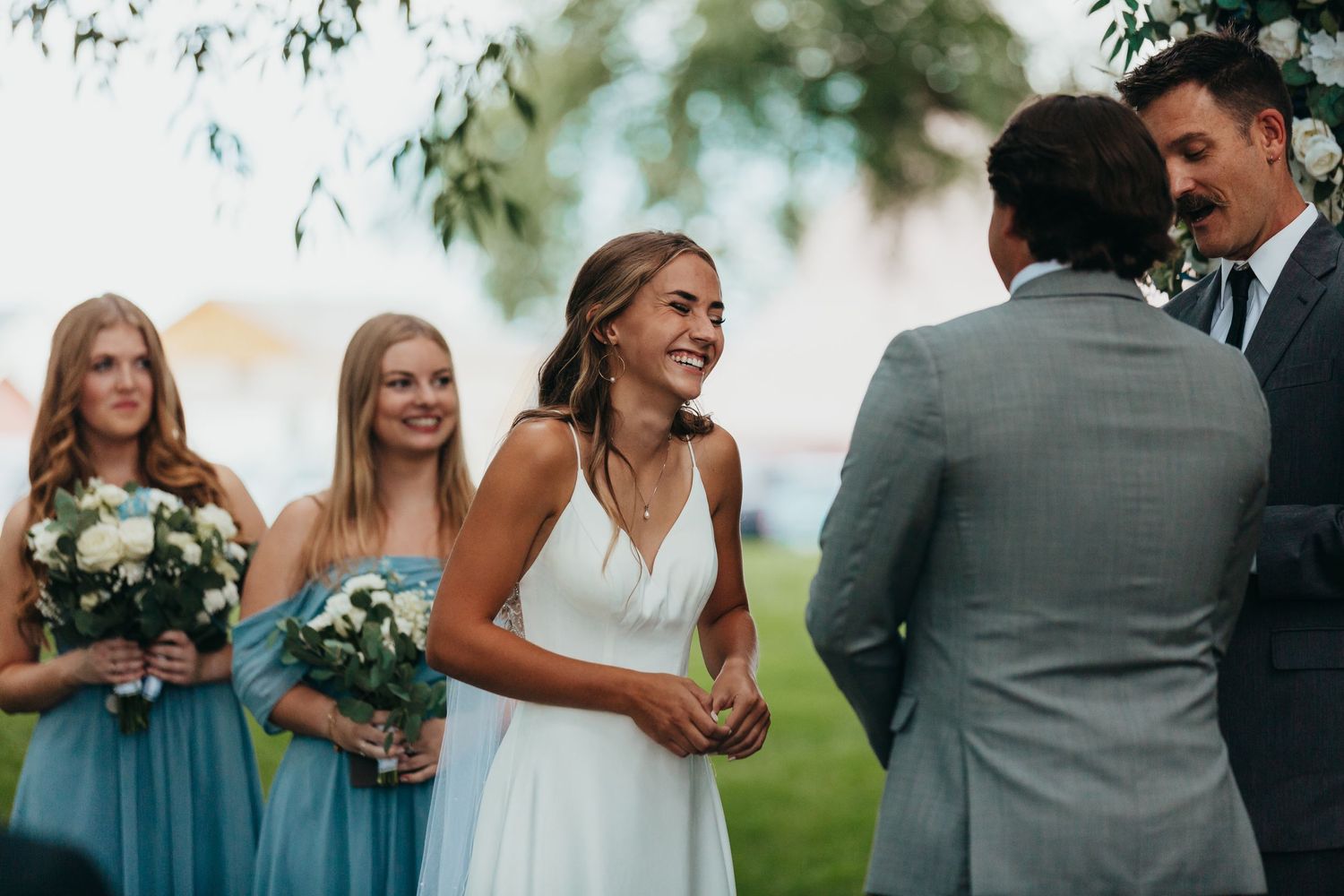Wedding party sharing a joyful moment during an outdoor ceremony with bridesmaids in blue dresses.