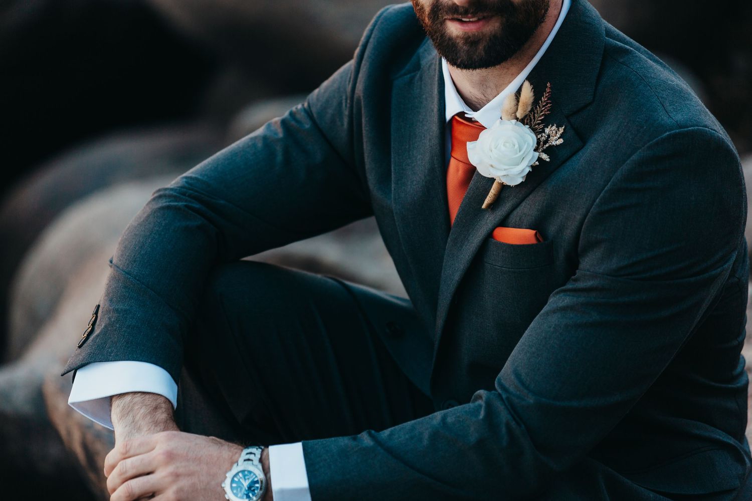 Close-up detail of a groom's navy suit with orange tie and white boutonniere.