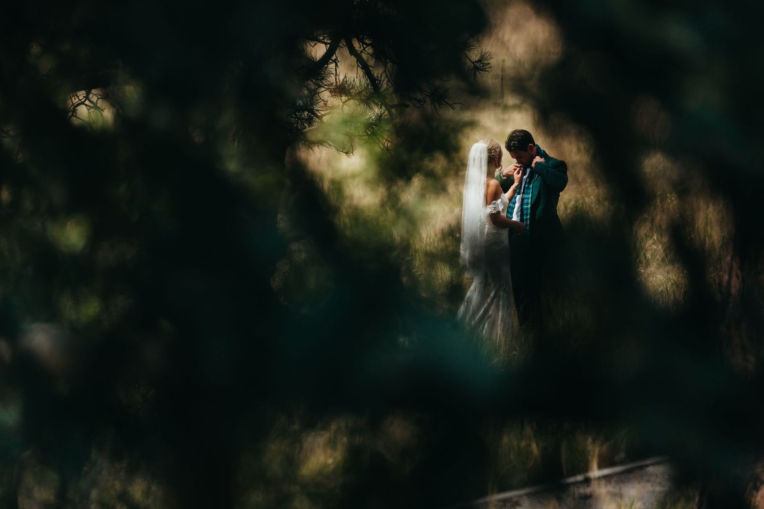 Romantic wedding couple embracing in dreamy forest setting with natural light filtering through trees.