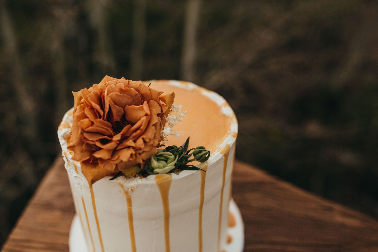White wedding cake decorated with orange rose and gold drip effect on wooden surface.