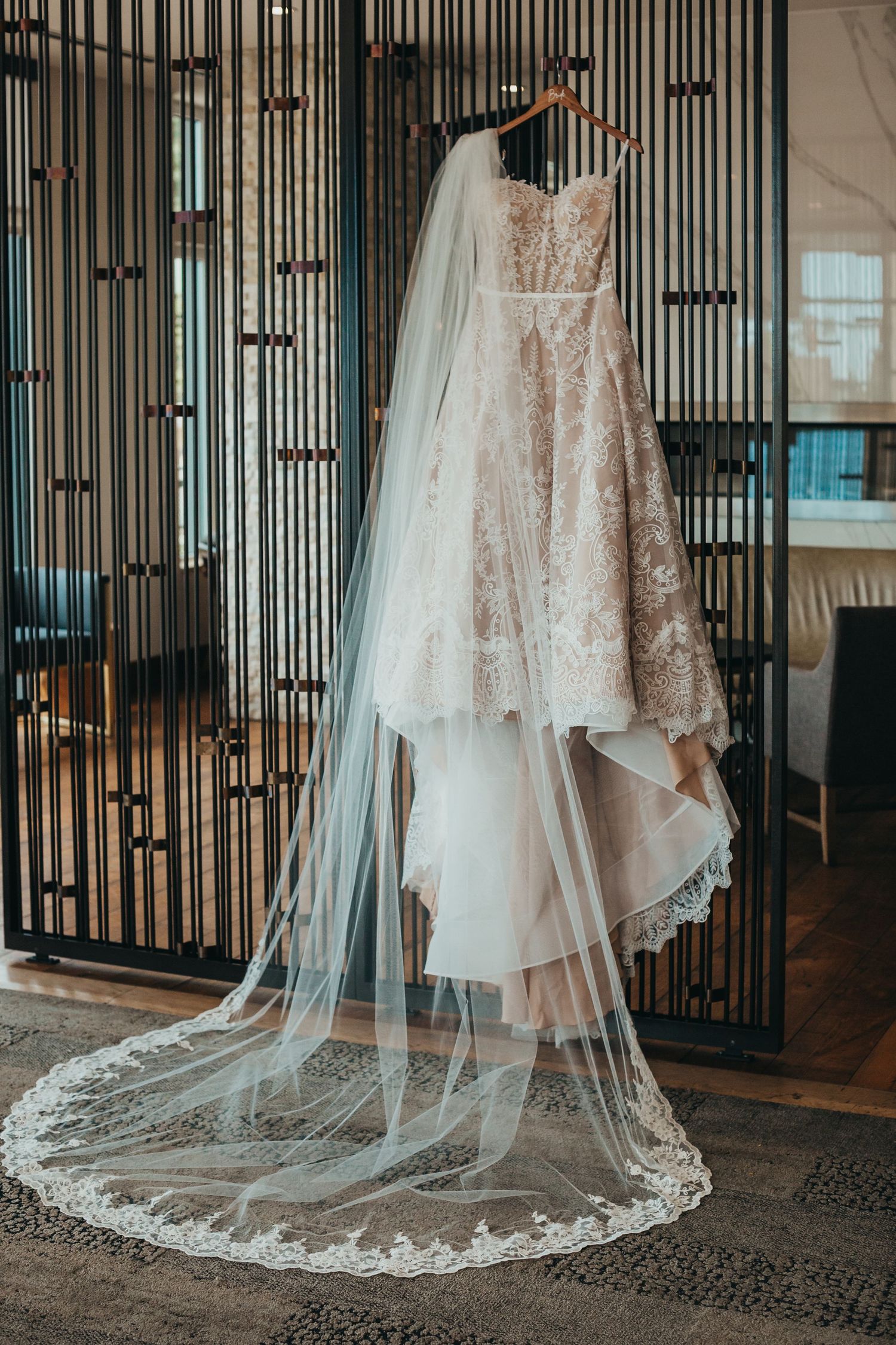 Elegant lace wedding dress with cathedral veil hanging on modern metal display.