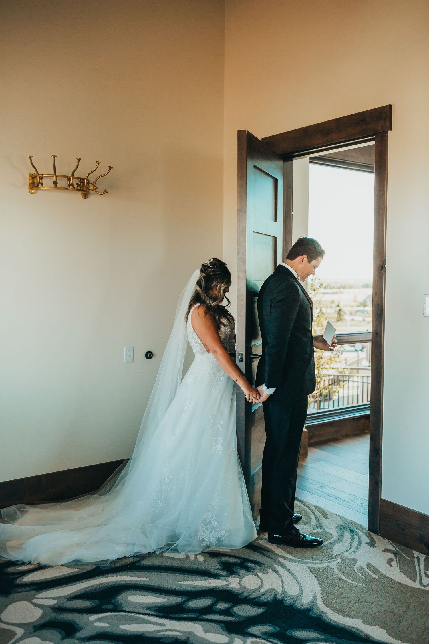 Bride and groom share a private moment while holding hands through a doorway before their ceremony.