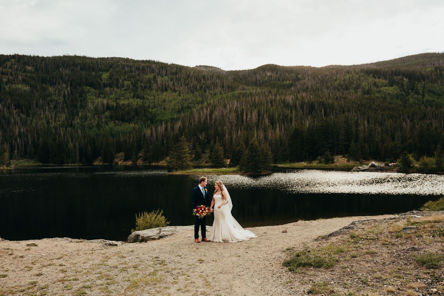 A wedding couple poses at a scenic mountain lake overlook.