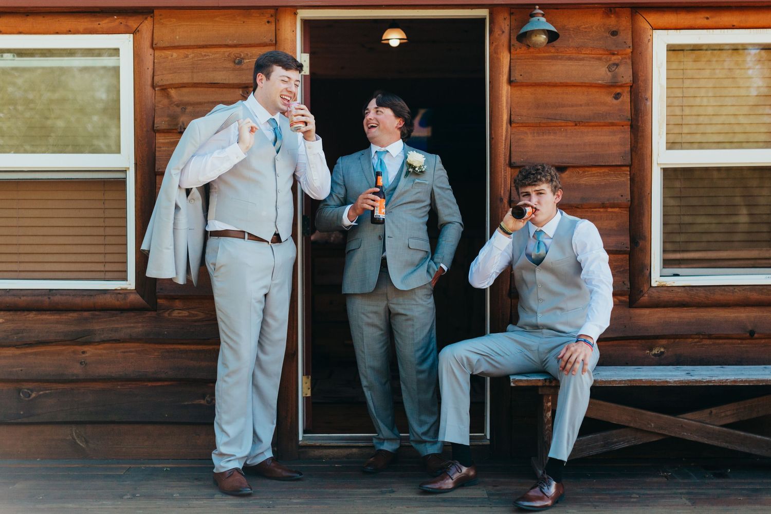 Three people in formal attire share drinks and laughs on rustic cabin porch.