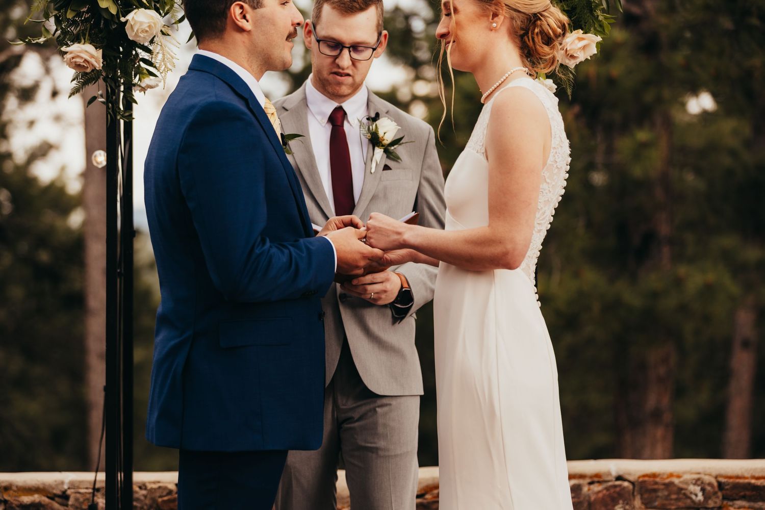 A couple exchanges wedding vows during an intimate outdoor ceremony with an officiant in grey.