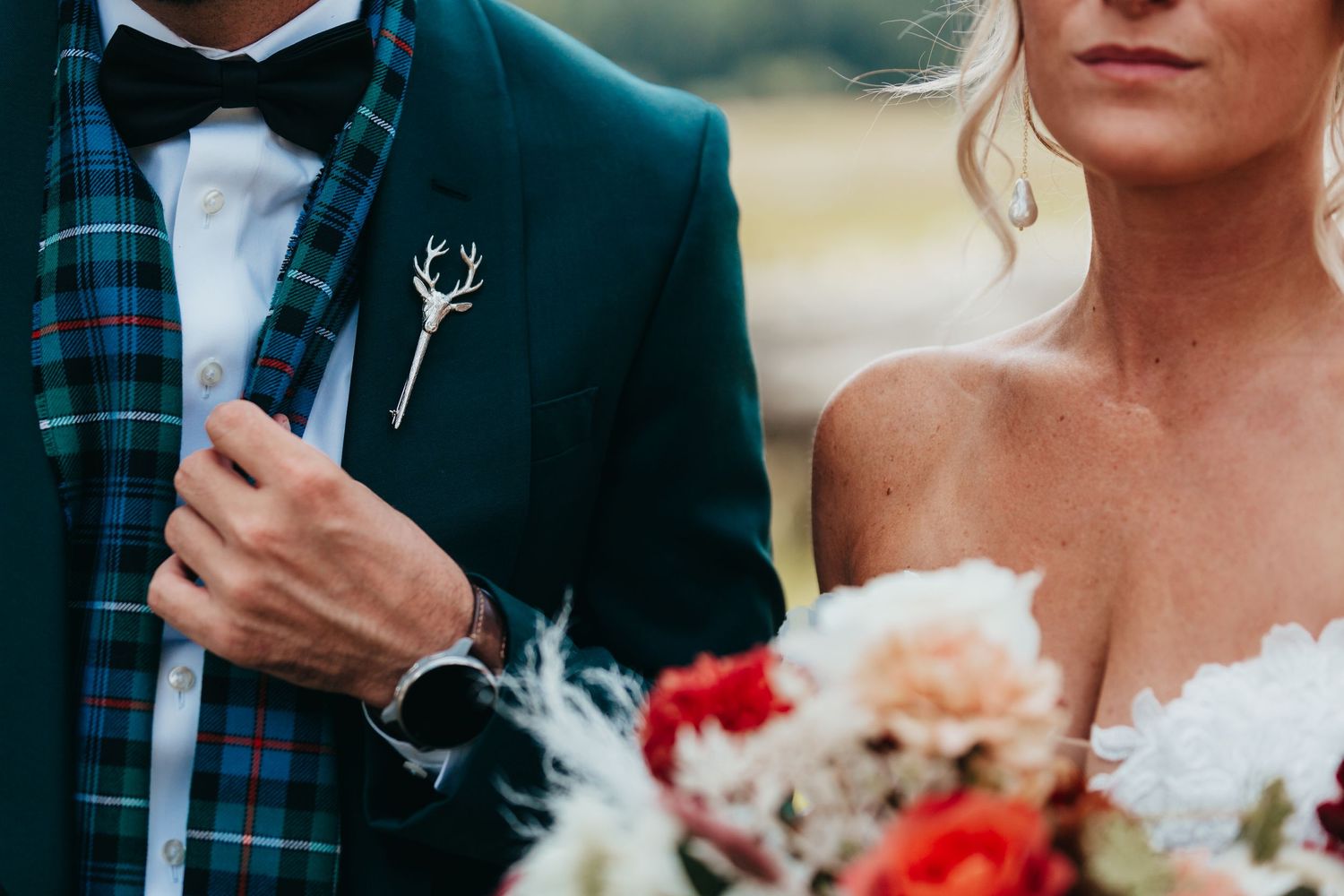 Close-up of plaid suit jacket with deer antler boutonniere and white floral bouquet.