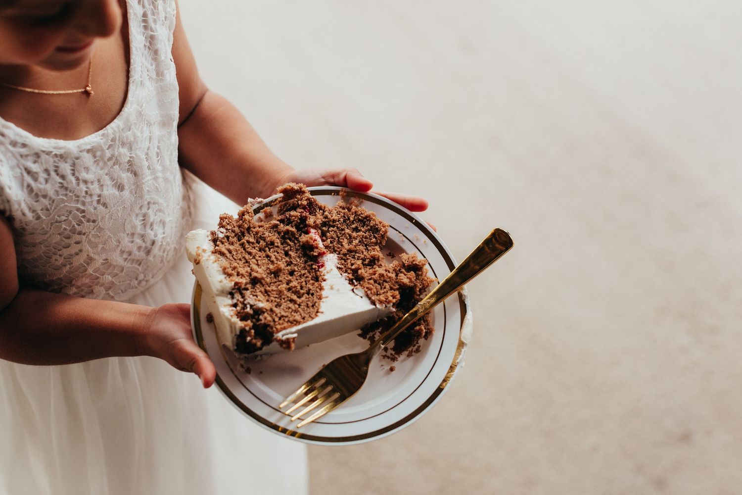 Hands holding a plate with a slice of chocolate layer cake and fork on white background.