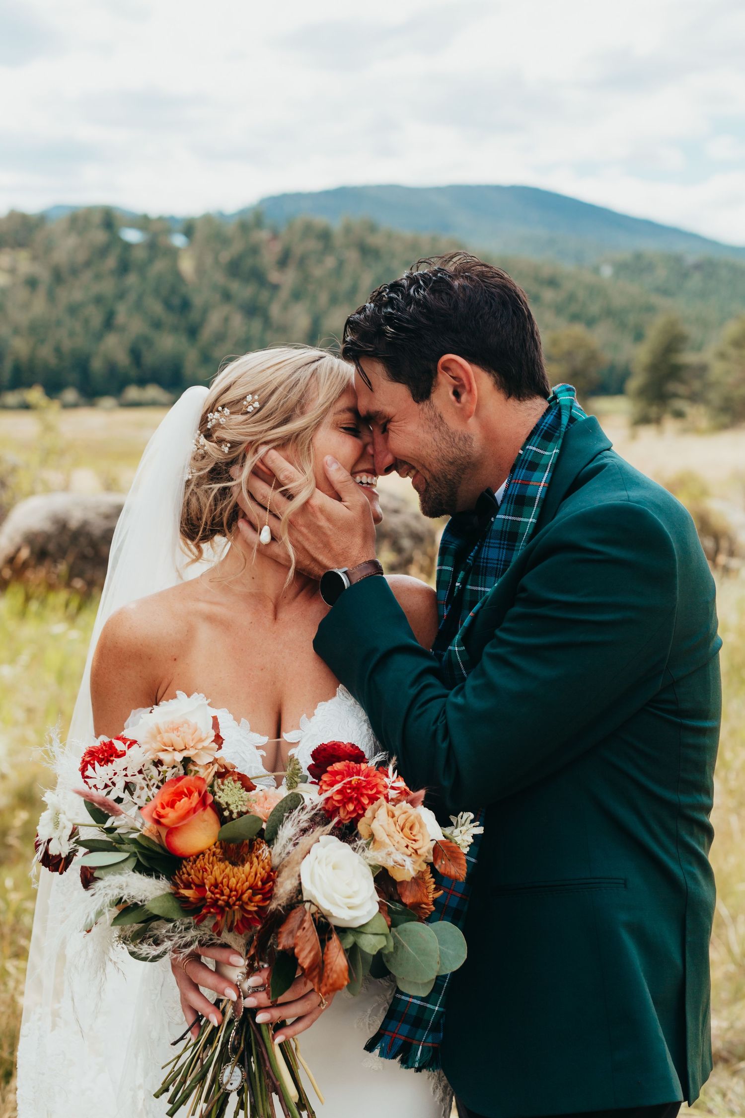 Tender moment between newlyweds with mountain landscape and fall bouquet.