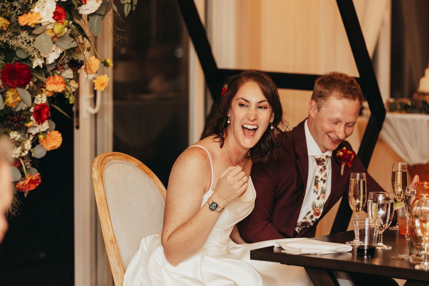 A couple sharing a joyful moment while seated at an elegantly decorated wedding reception table.