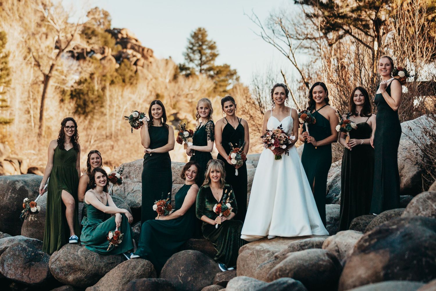 Wedding party of bridesmaids in dark dresses arranged on rocky terrain.