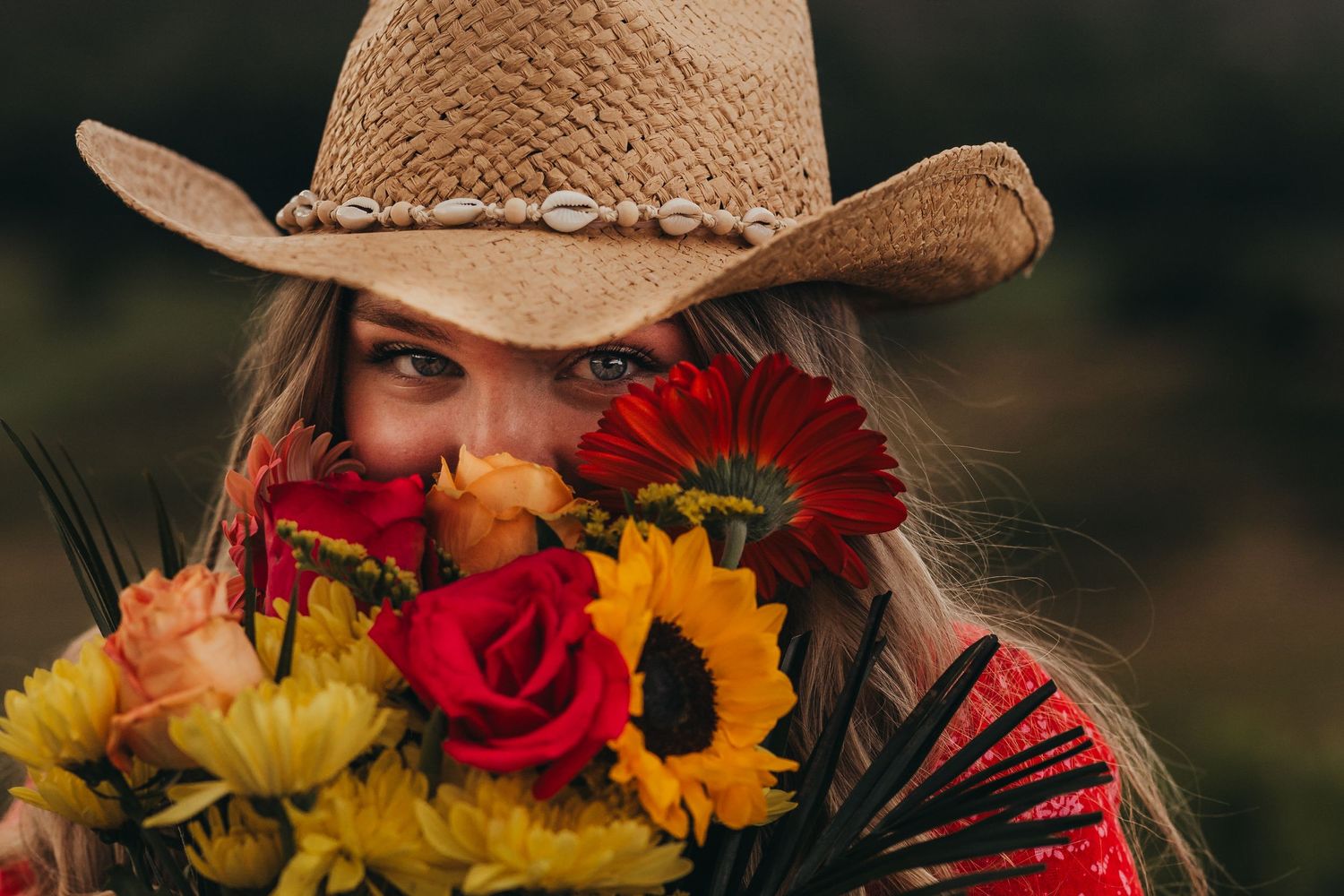 Portrait of person in cowboy hat holding colorful bouquet with roses and sunflowers.