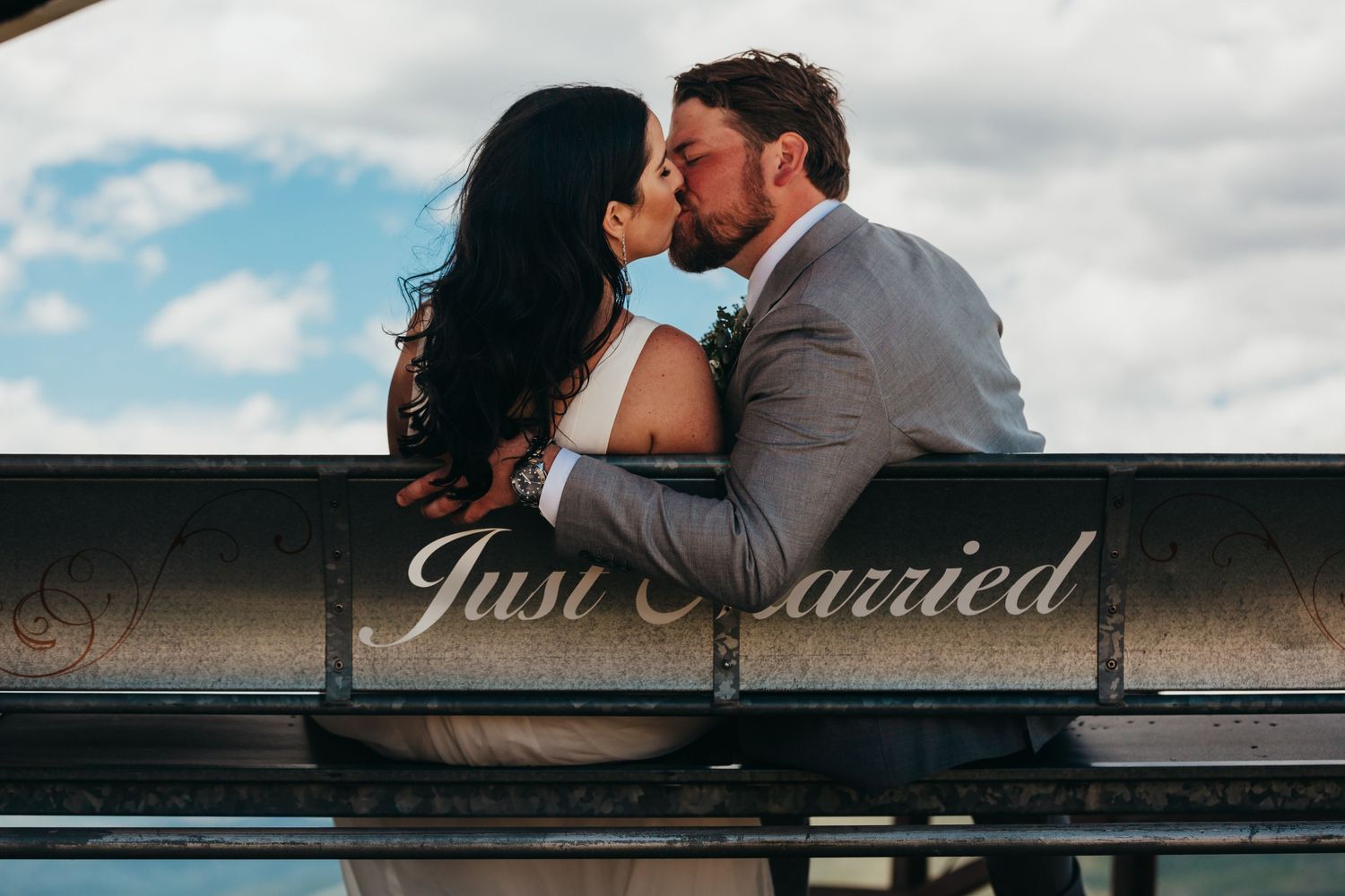 A romantic moment captured beneath a 'Just Married' sign with cloudy skies in the background.