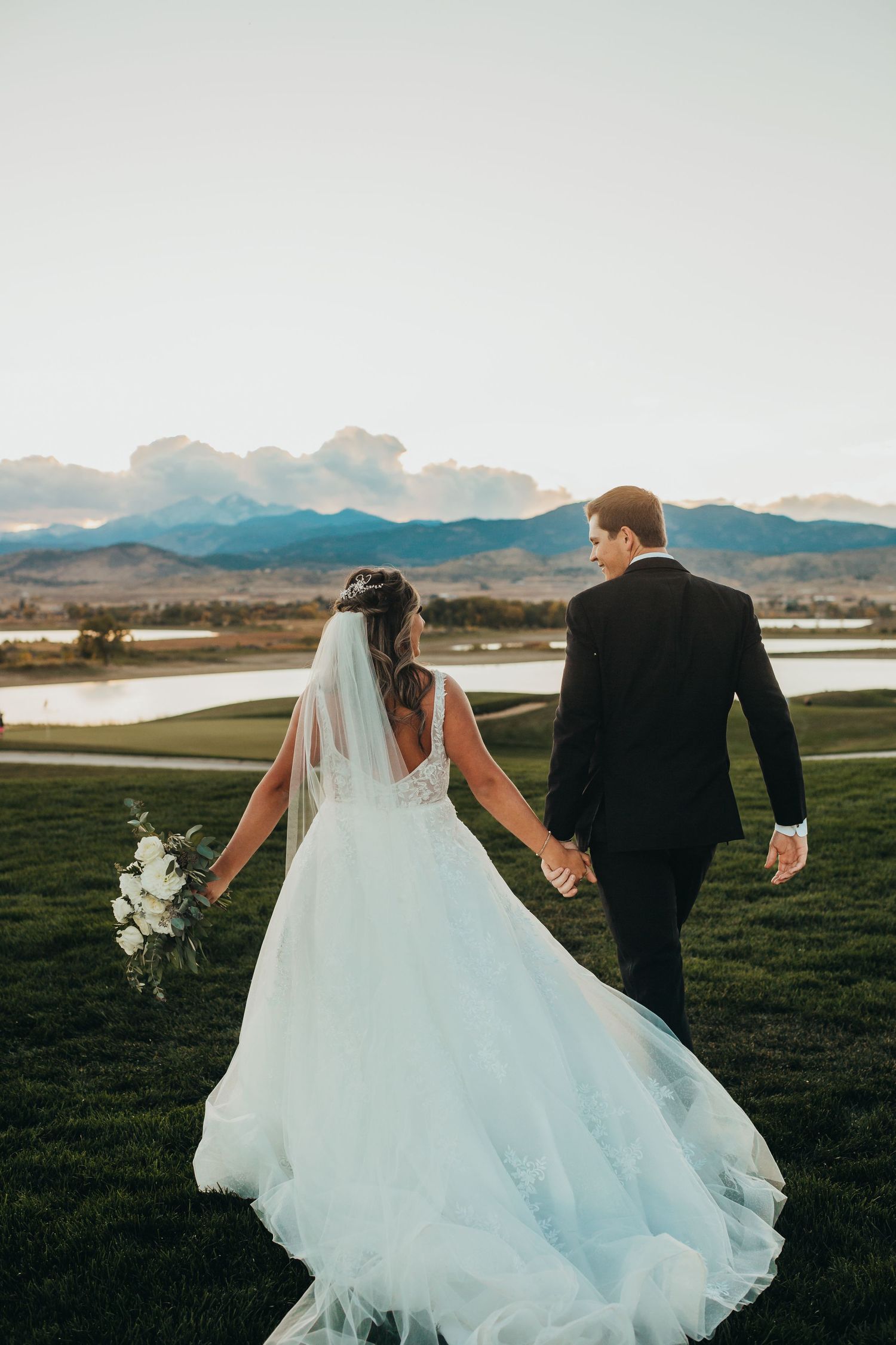 Newlyweds walking hand in hand with mountain landscape in background.