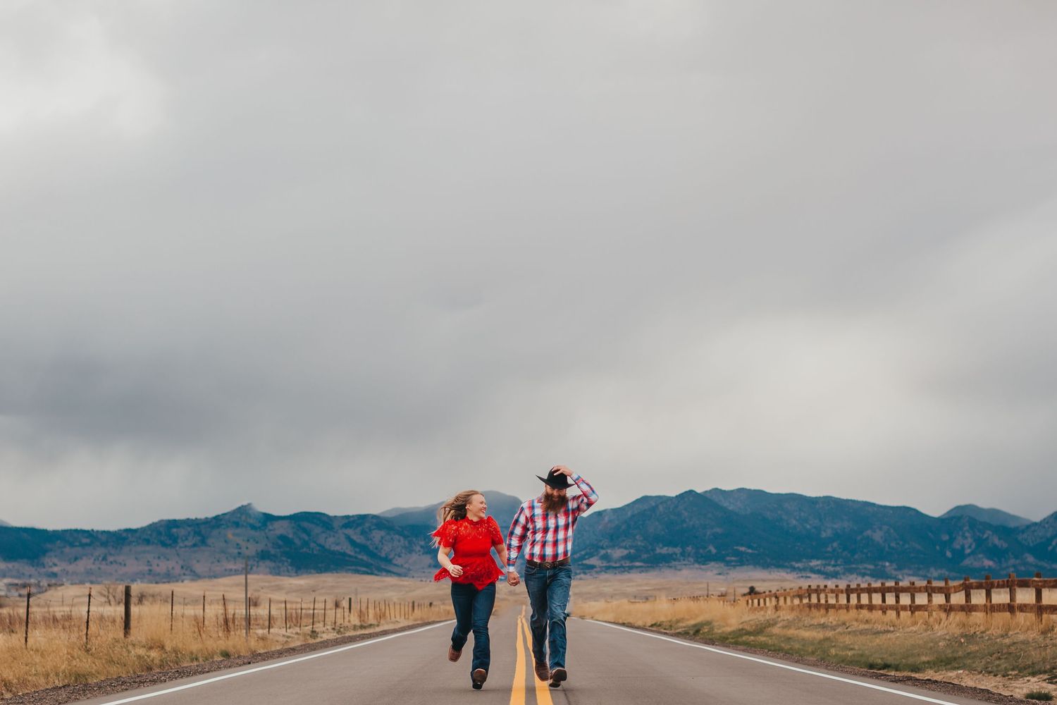 A couple walks down a rural road with mountains in the distance under stormy skies.