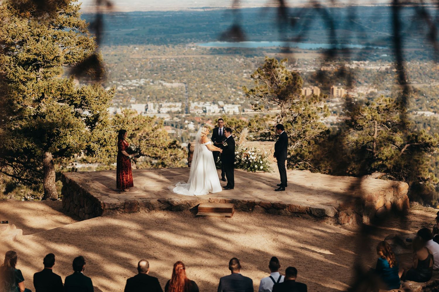 A mountaintop wedding ceremony with guests watching from wooden benches against a scenic valley view.