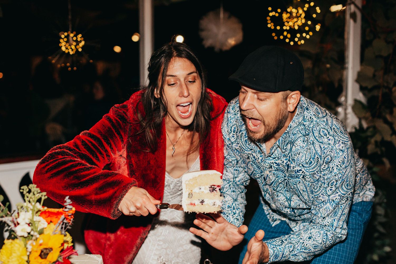 Wedding couple shares a joyful moment while cutting cake at their reception celebration.