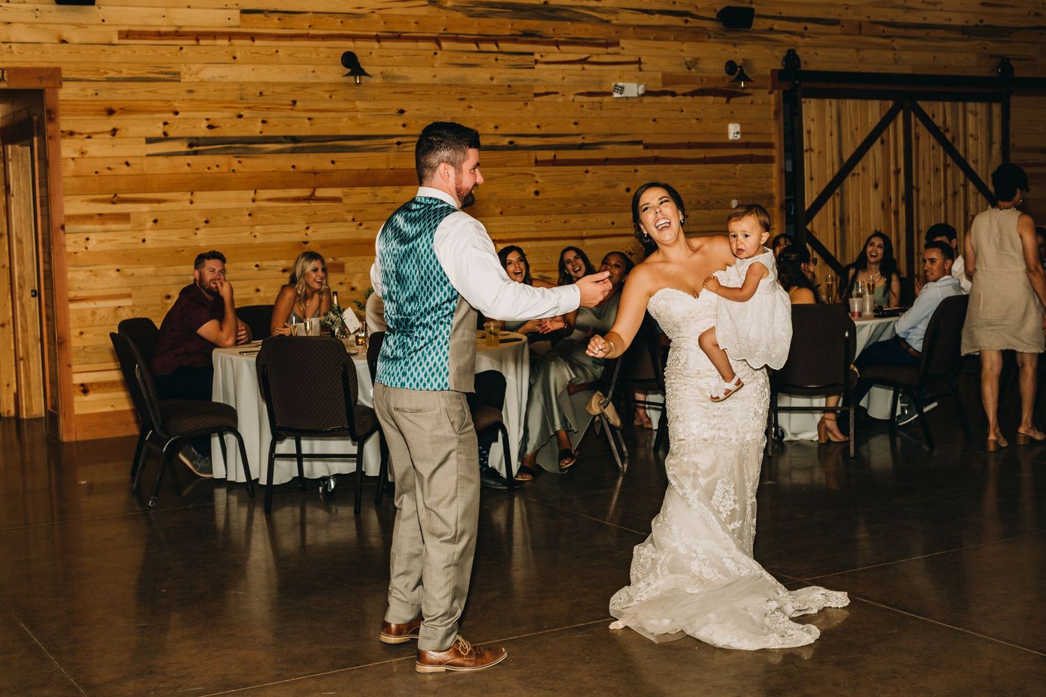A dancing scene unfolds on a wooden floor in a rustic barn reception venue.
