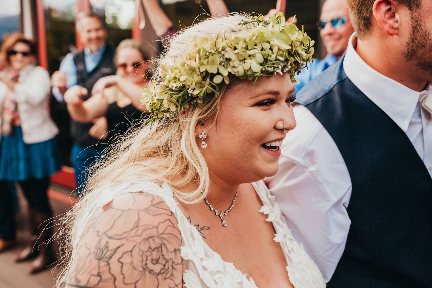 A person wearing a floral crown and lace dress smiles during an outdoor wedding celebration.