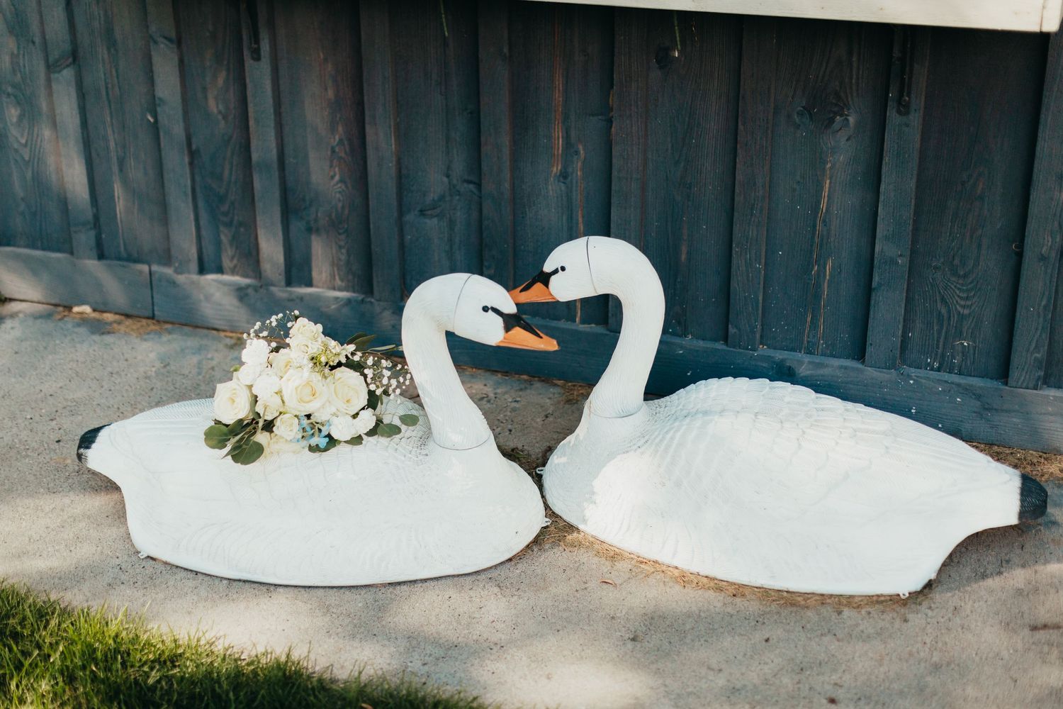 Two decorative white swan figures with floral arrangements against dark wooden wall.