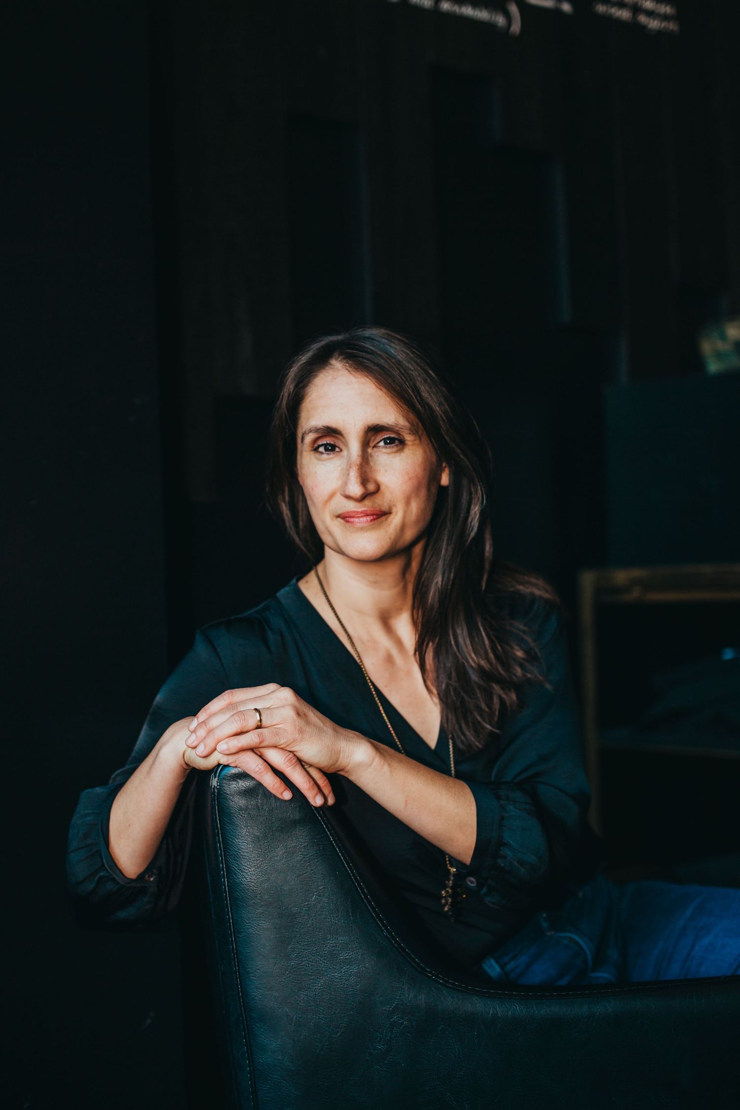 Professional portrait of someone seated in dark setting with moody lighting.