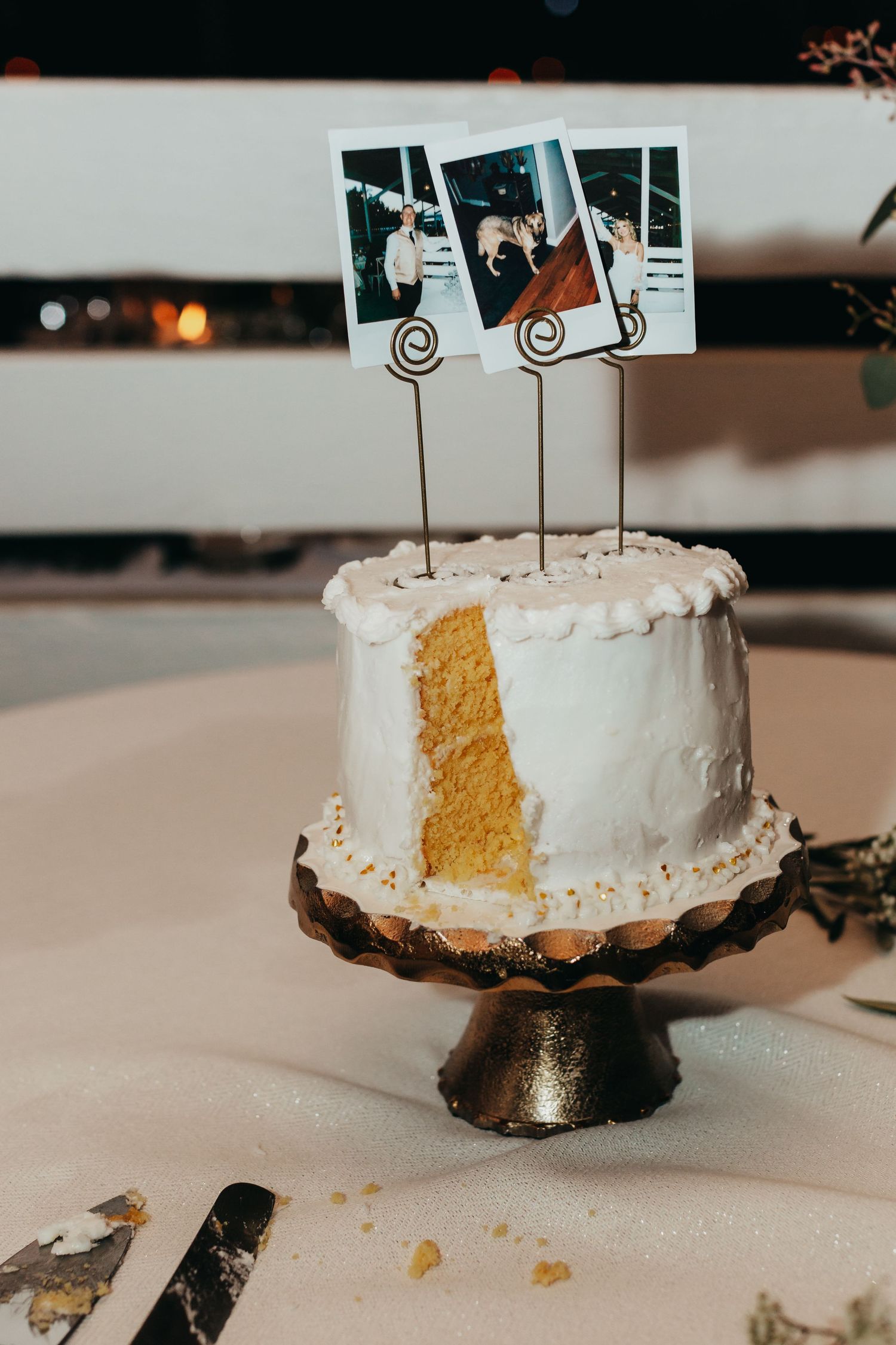White wedding cake with photos displayed on wire holders revealing a golden interior on a metal cake stand.