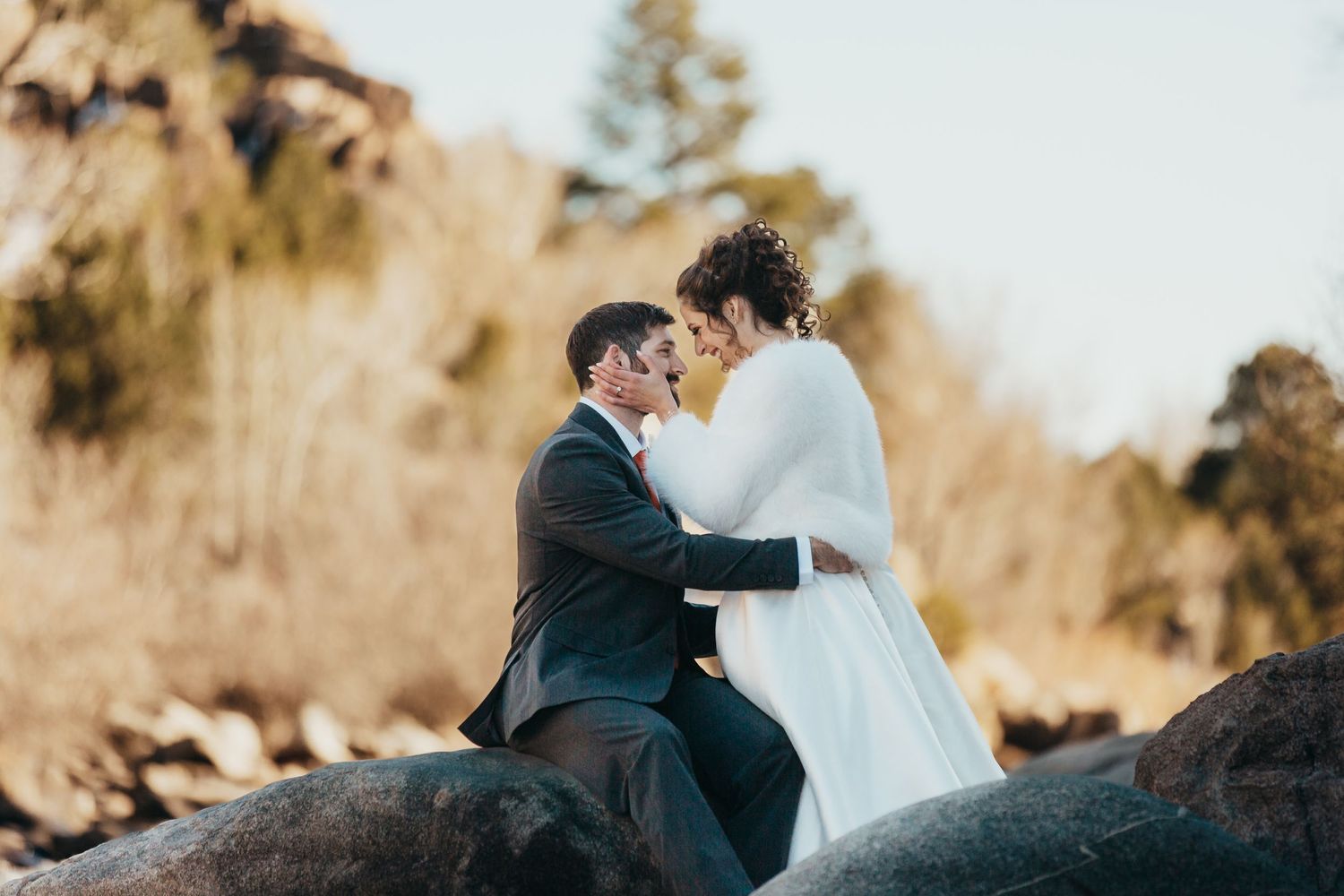 Couple shares intimate moment while sitting on coastal rocks.