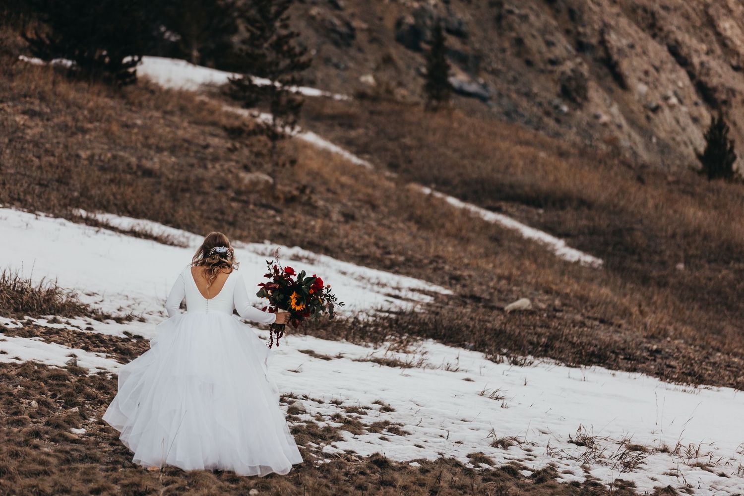 Person in white wedding dress holding bouquet in snowy mountain landscape.