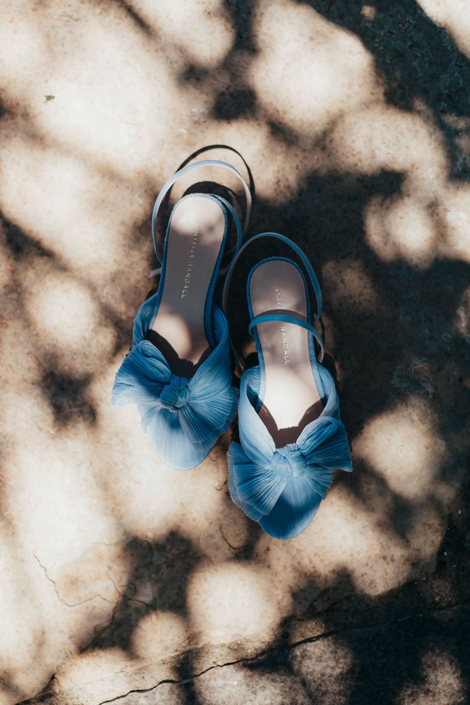 Blue satin bridal shoes with bow detail photographed in dappled light.