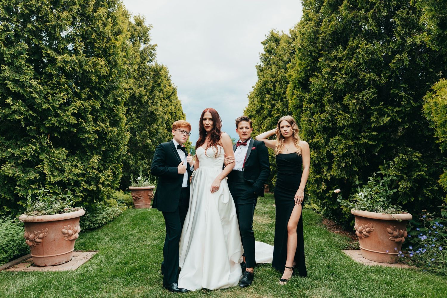 Wedding party poses in garden path with large terracotta planters on a sunny afternoon.