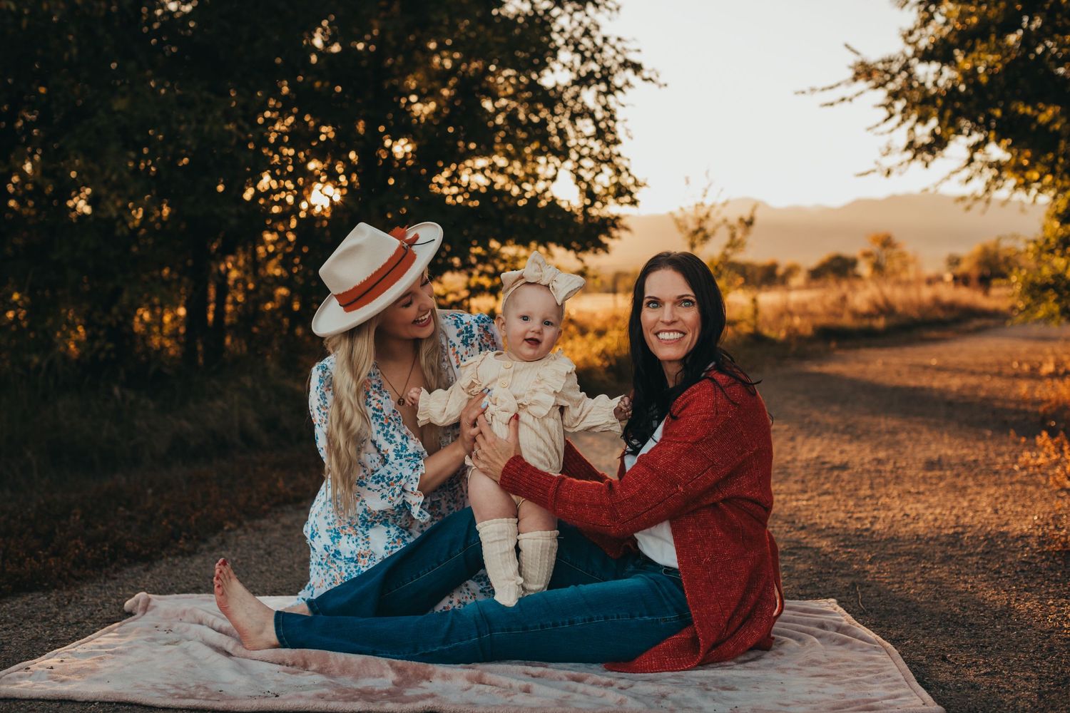 Three people sit together on a blanket during golden hour sunset in nature.