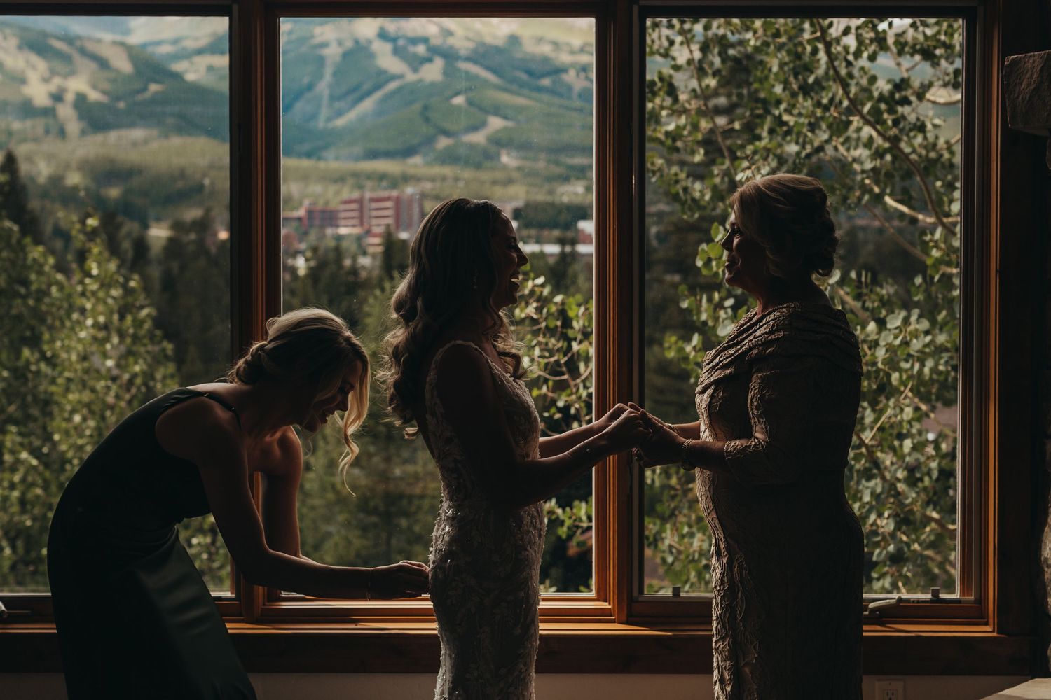 A silhouetted pre-wedding scene with getting ready activities against large mountain view windows.