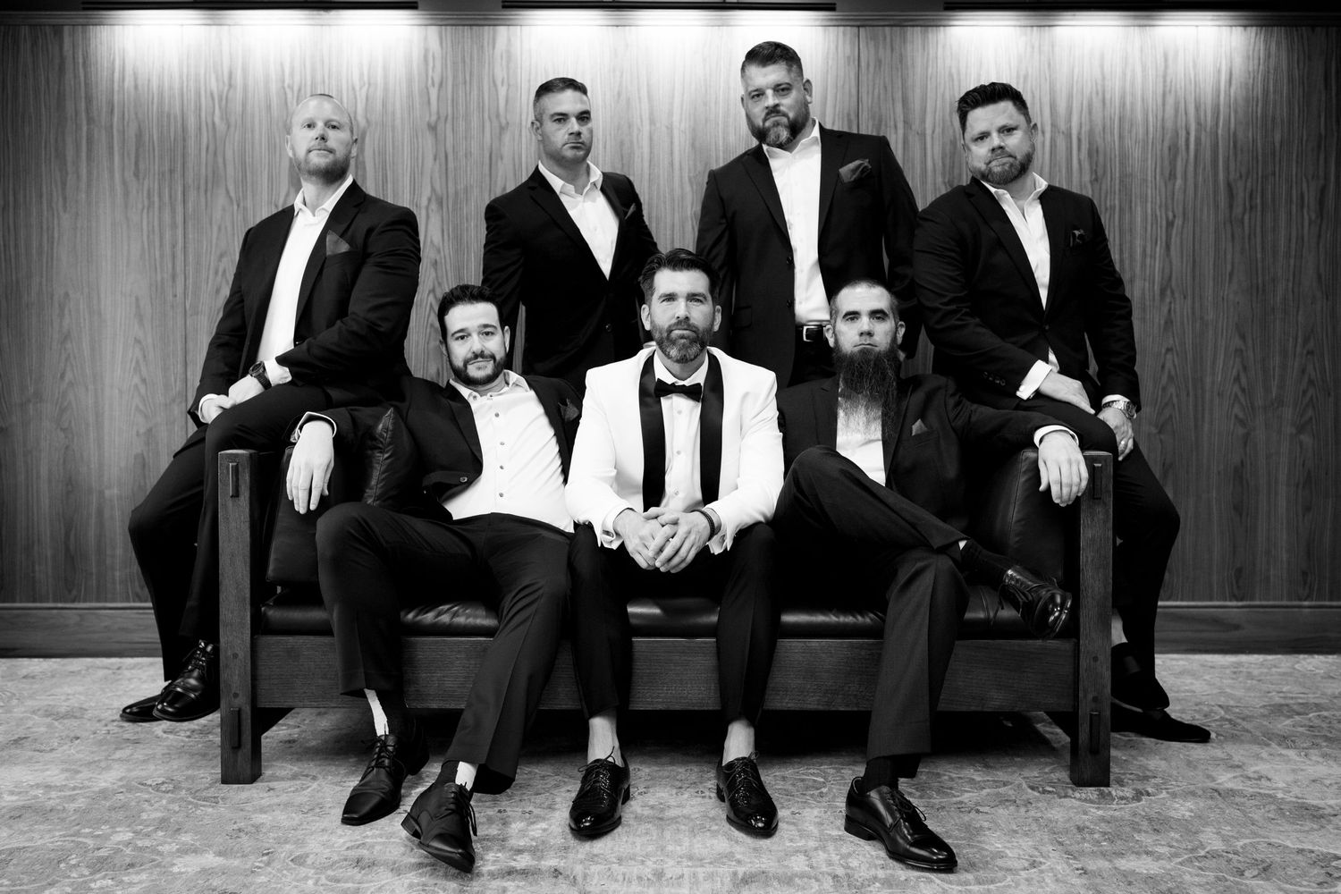 A group of men in formal attire pose together on a couch for a dramatic portrait.