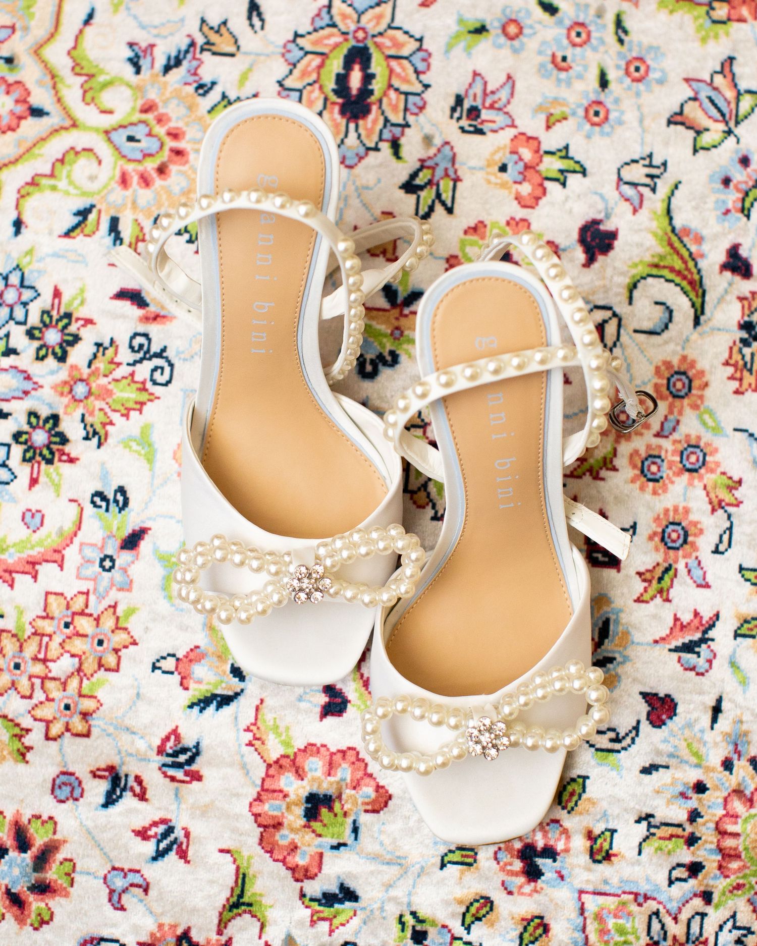 Elegant white bridal shoes with pearl details displayed on a colorful floral patterned fabric.