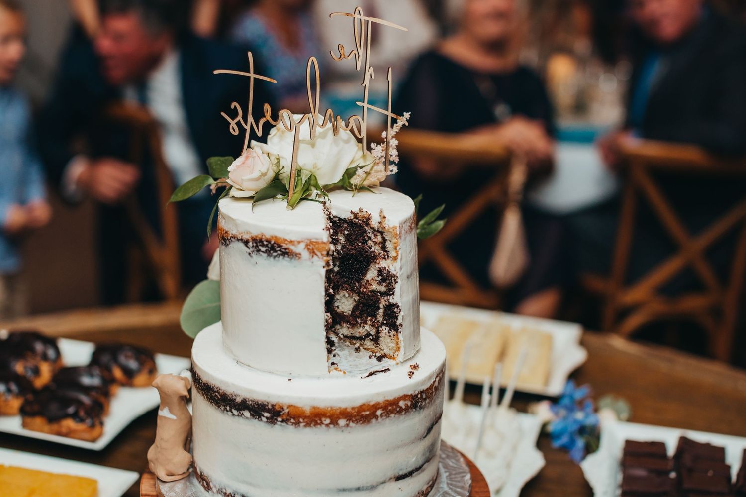 Rustic semi-naked wedding cake decorated with white flowers and metallic toppers.