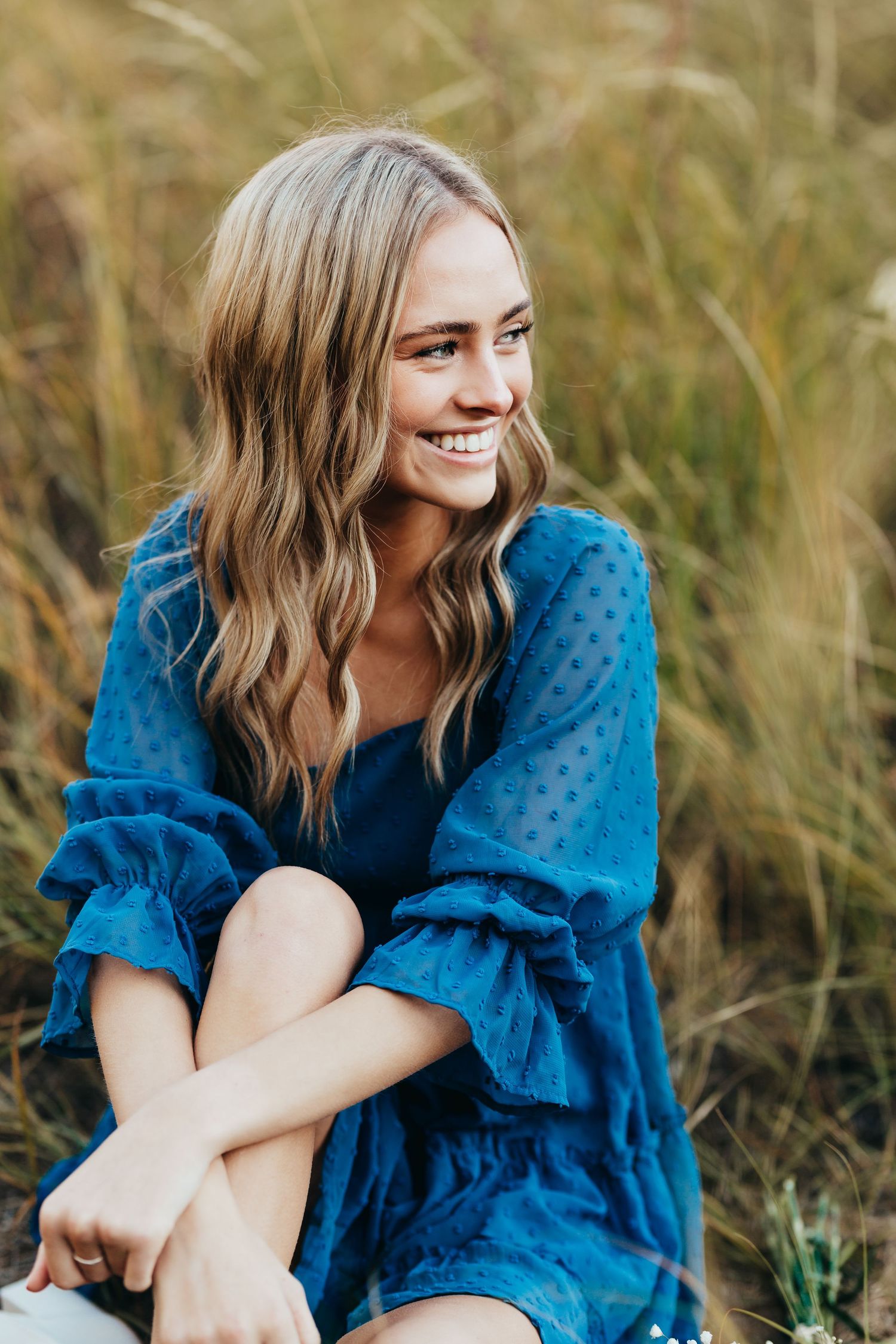Portrait of someone in a blue polka dot dress sitting in tall grass.