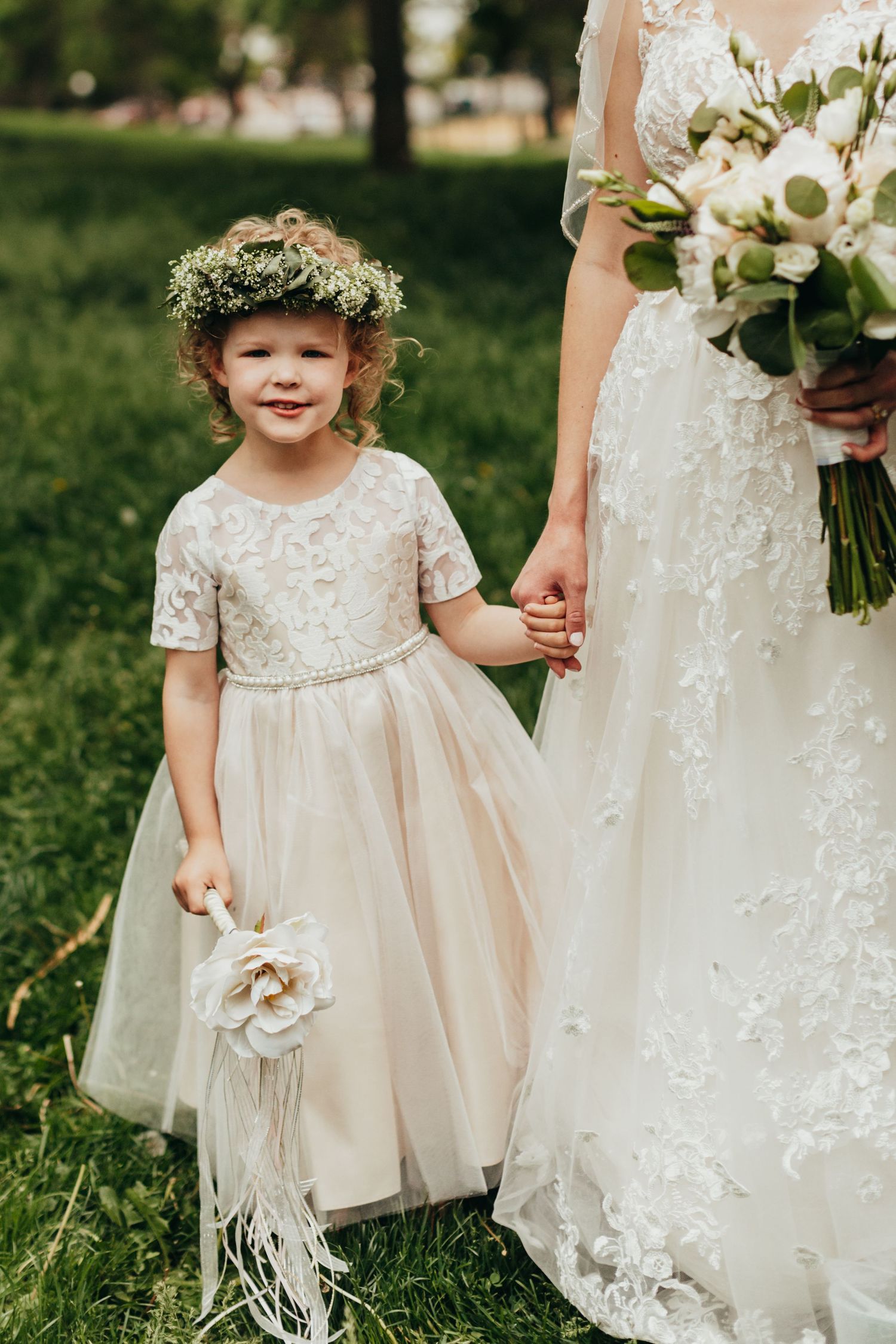 A flower girl in lace dress holds the bride's hand while carrying a small bouquet.