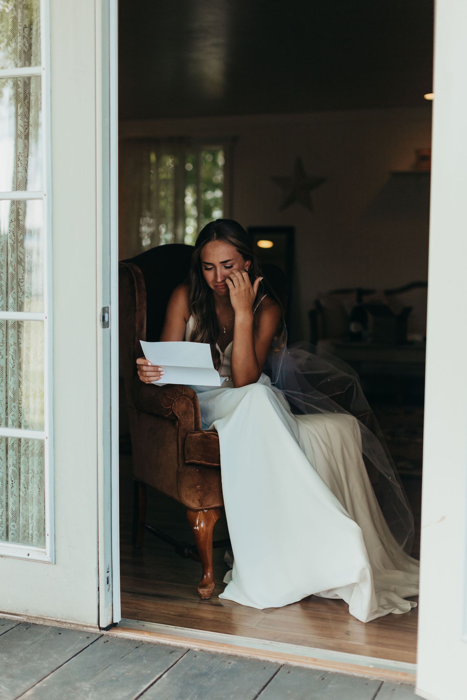 Wedding dress visible through open french doors as someone reads at indoor seating area.