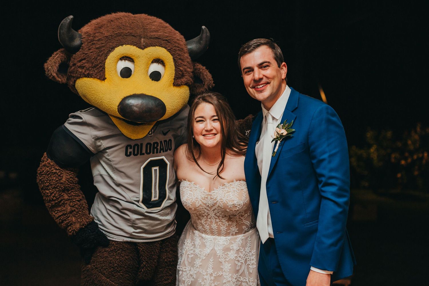 Wedding couple poses with Colorado mascot Buffalo wearing team jersey at reception.